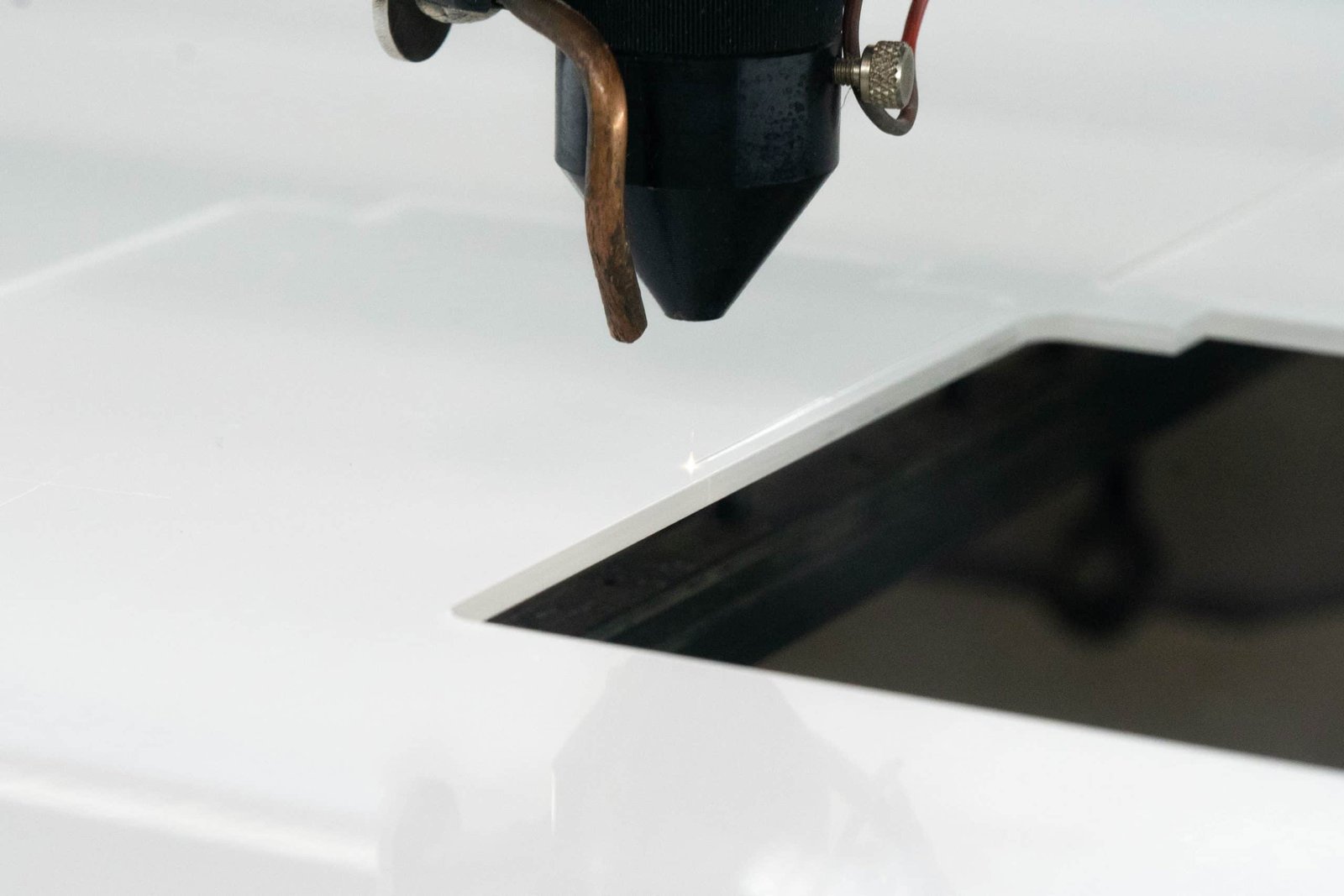 Close-up of a laser cutting machine's nozzle precisely cutting white acrylic material, with a bright spark at the point of contact.