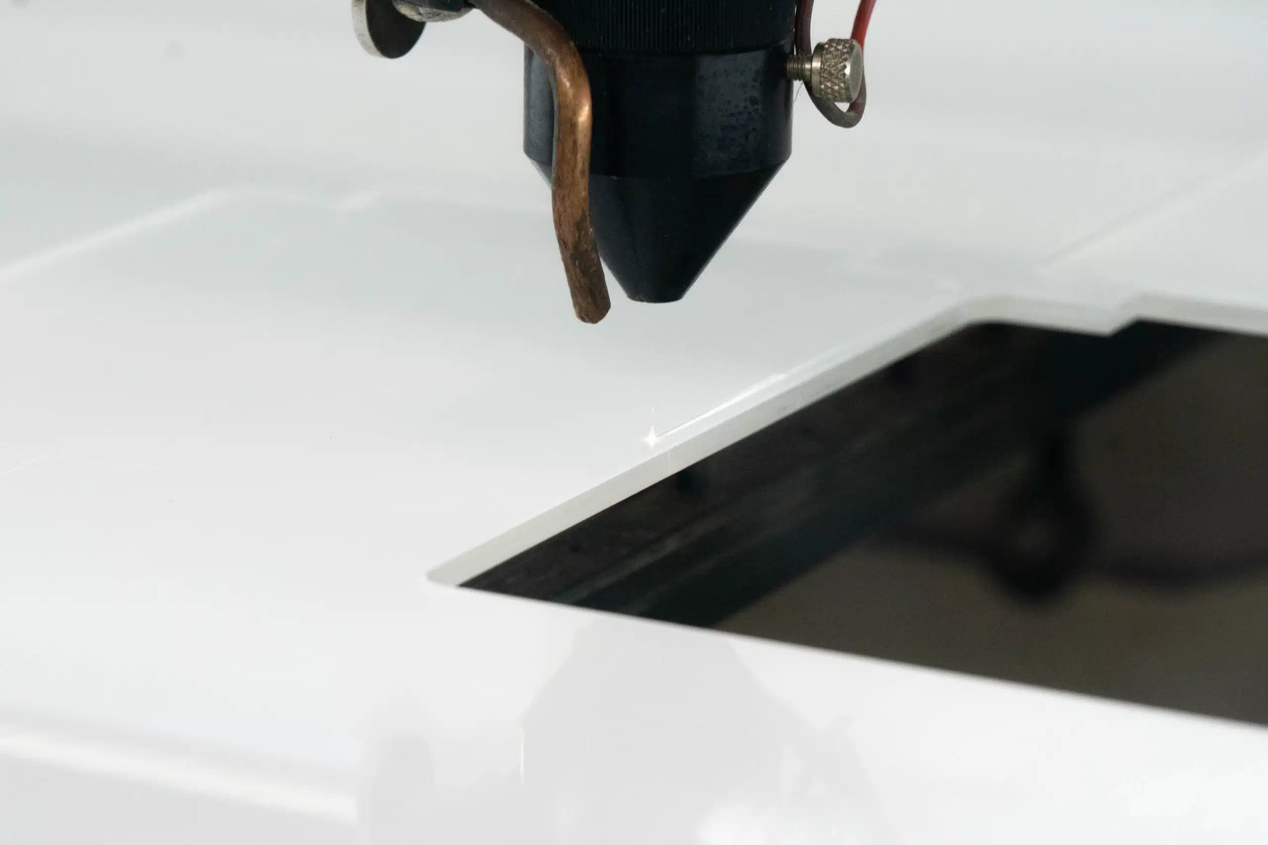 Close-up of a laser cutting machine's nozzle precisely cutting white acrylic material, with a bright spark at the point of contact.