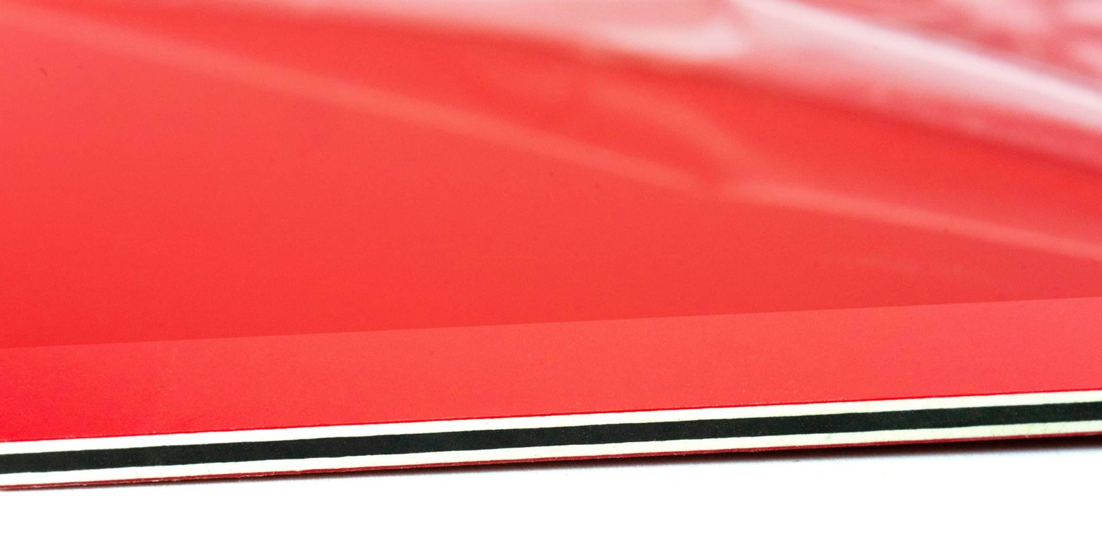 Close-up of a vibrant red Traffolyte, with a distinct horizontal black and thin white stripe along its bottom edge.