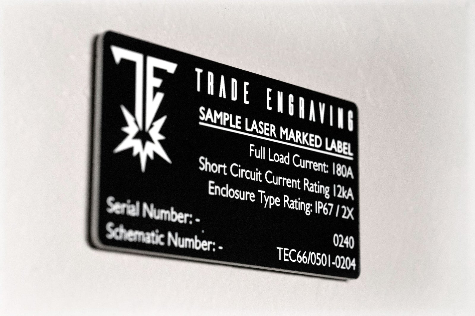 A detailed black laser-marked industrial label from Trade Engraving, displaying 'Full Load Current: 180A' and 'IP67' rating.