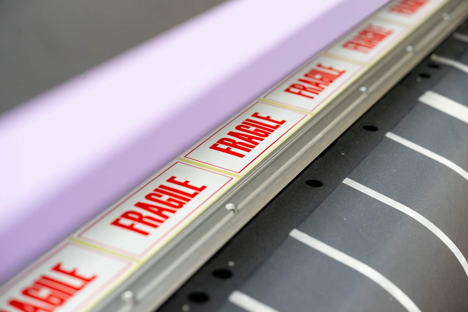 Close-up of a roll of white and red 'FRAGILE' warning labels being fed through an industrial printing or labelling machine.