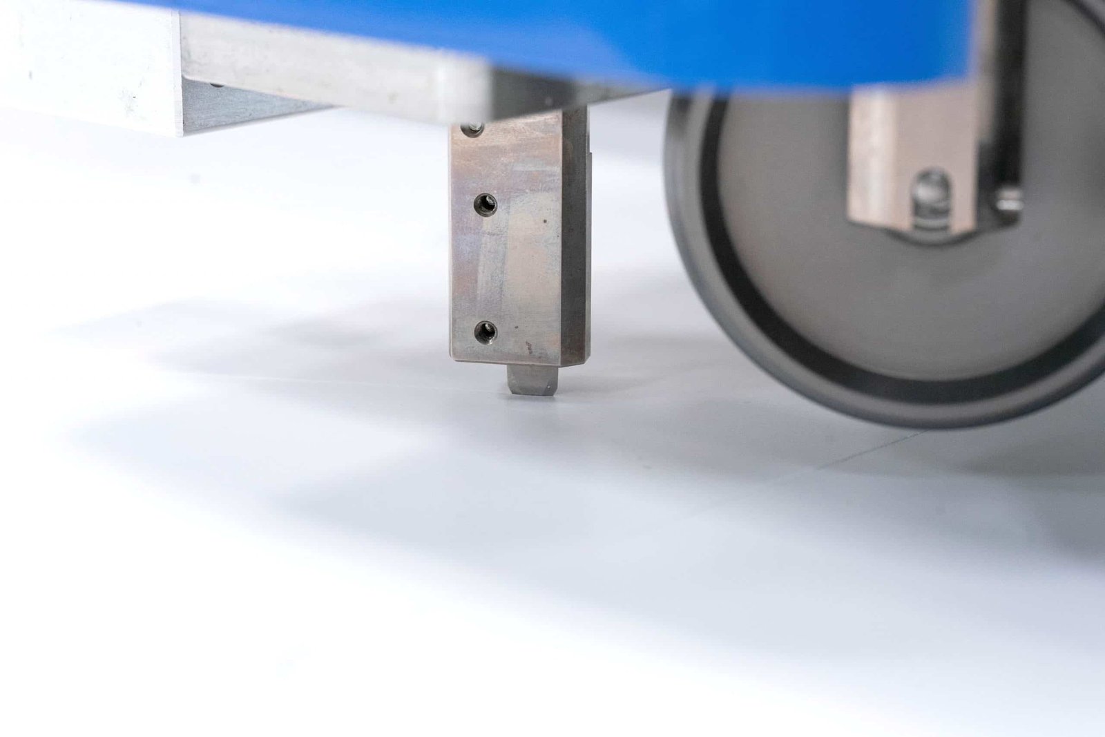 Close-up of a high-precision industrial machine component, showing a metallic arm with a tip hovering over a white surface, and a blurred wheel. Represents automation and modern manufacturing.