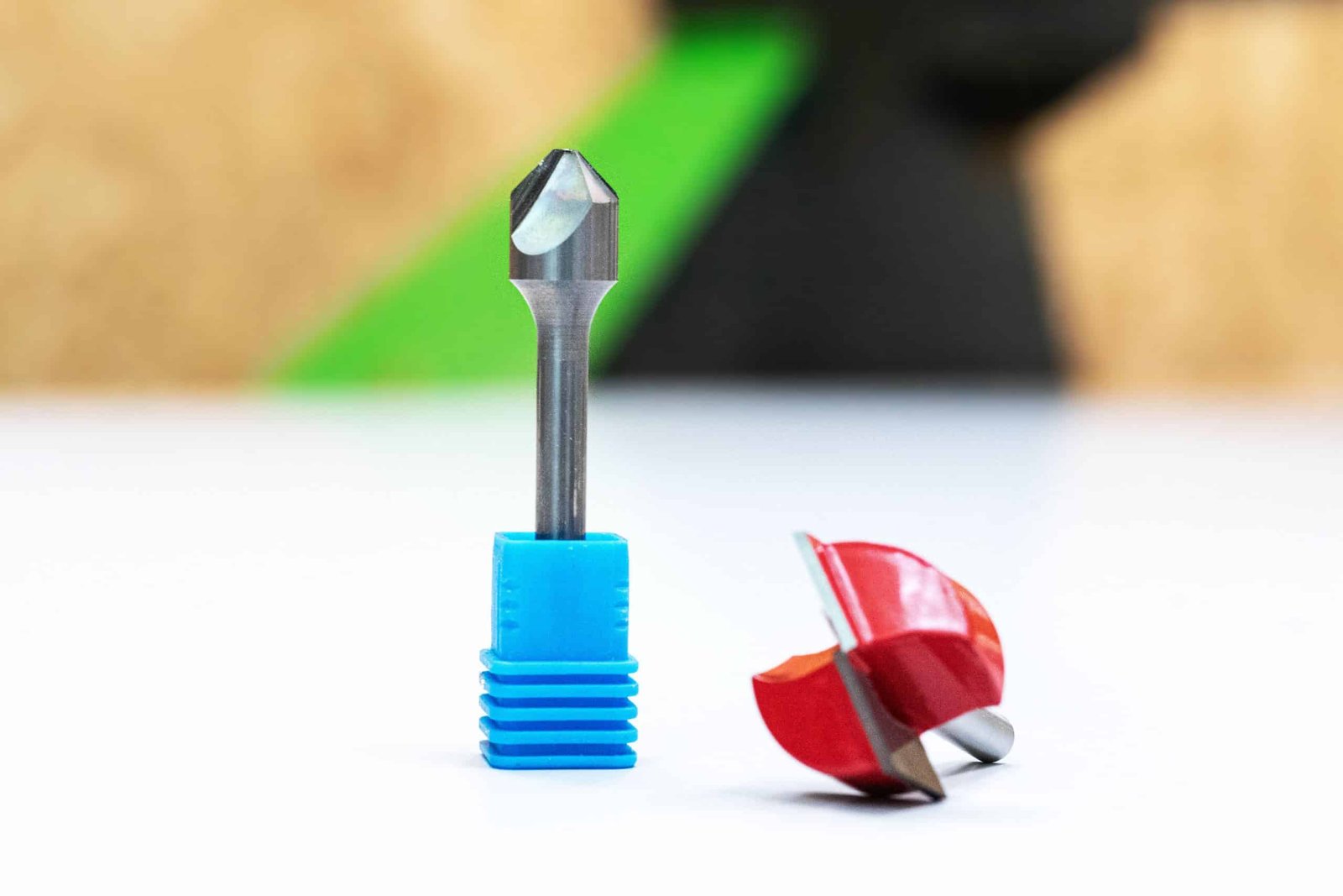 Two CNC router bits on a white surface: a V-groove bit standing upright in a blue sleeve and a red round-over bit.