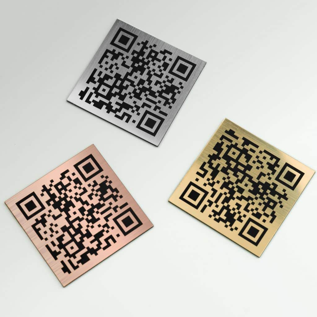 Three metallic QR code plates on a white background: one silver, one bronze, and one gold, all with brushed finishes.