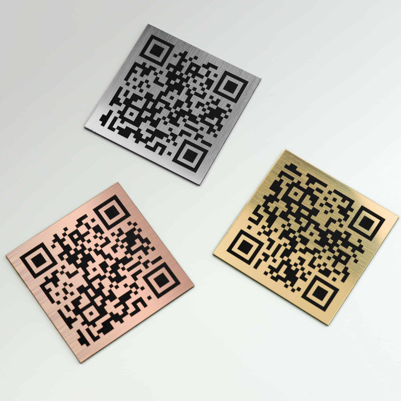 Three metallic QR code plates on a white background: one silver, one bronze, and one gold, all with brushed finishes.