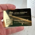 Hand holding a sleek gold metal Arrow Meadow Lifetime Member card with a fish logo and QR code for exclusive fisheries access.