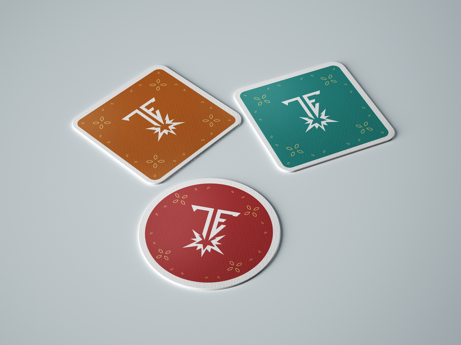 Three custom drink coasters in red, orange, and teal with a white 'TE' logo and starburst design, arranged on a light gray surface.