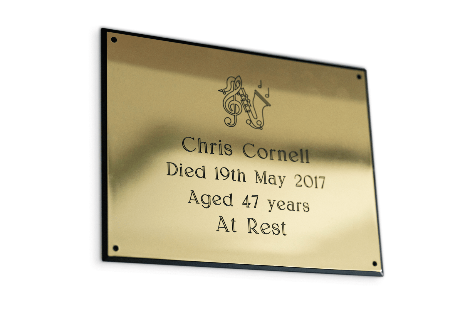 A golden brass memorial plaque for musician Chris Cornell, featuring engraved black text, a musical motif, and "Died 19th May 2017 Aged 47 years At Rest."