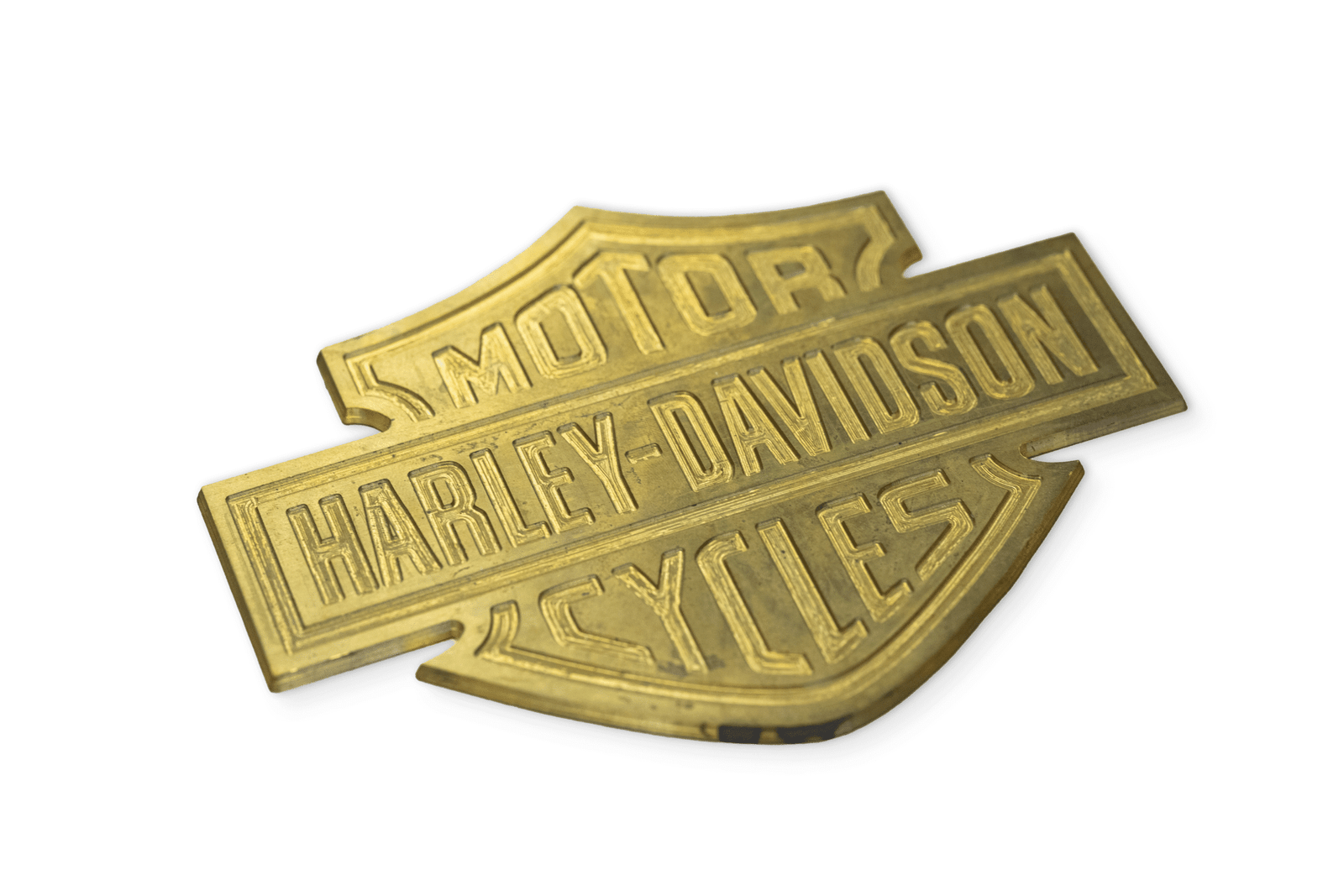 A vintage, brass Harley-Davidson Motor Cycles shield-shaped emblem, rotary engraved on solid brass, isolated on a clean white background.