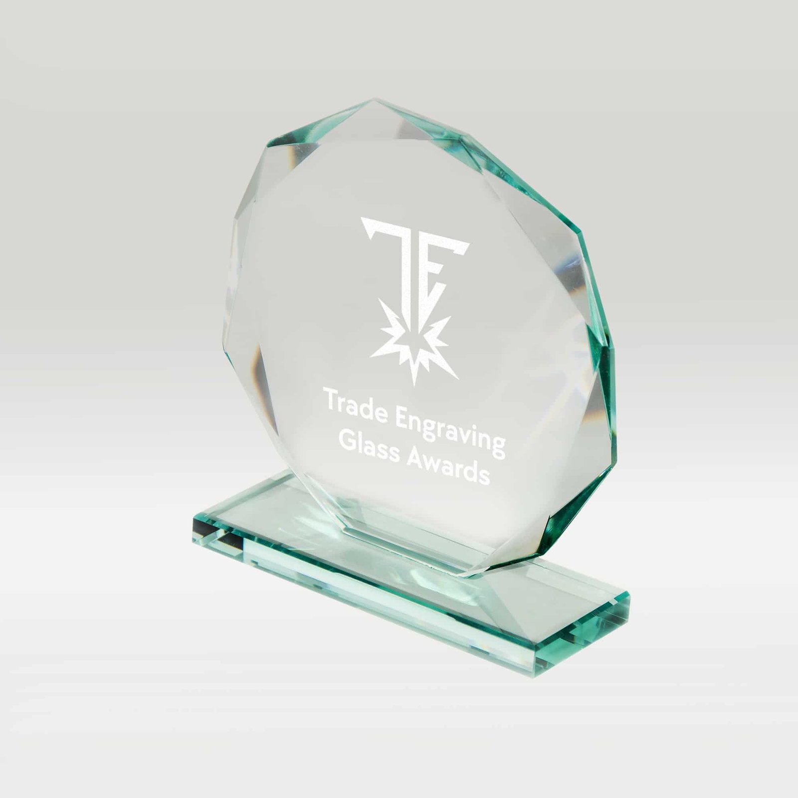 A clear, faceted glass award with 'Trade Engraving Glass Awards' text and 'TE' logo engraved, set against a light background.